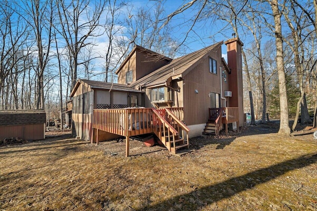 rear view of house featuring a wooden deck, an outdoor structure, a chimney, and a sunroom