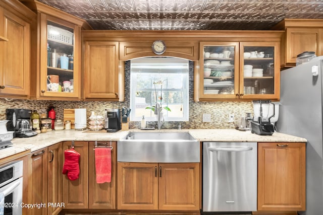 kitchen featuring a sink, appliances with stainless steel finishes, decorative backsplash, brown cabinets, and an ornate ceiling