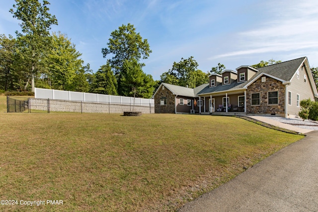 view of front of home featuring covered porch, stone siding, a front lawn, and fence