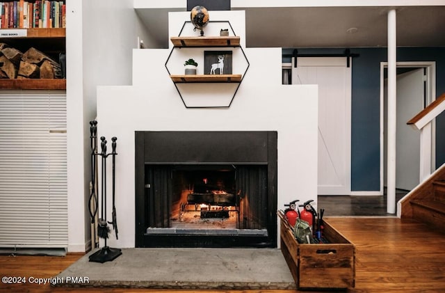 details featuring a warm lit fireplace, wood finished floors, and a barn door