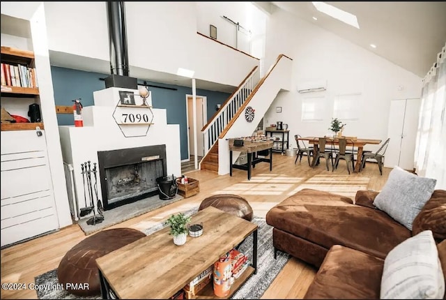 living room with a fireplace with raised hearth, high vaulted ceiling, wood finished floors, stairs, and a wall mounted air conditioner