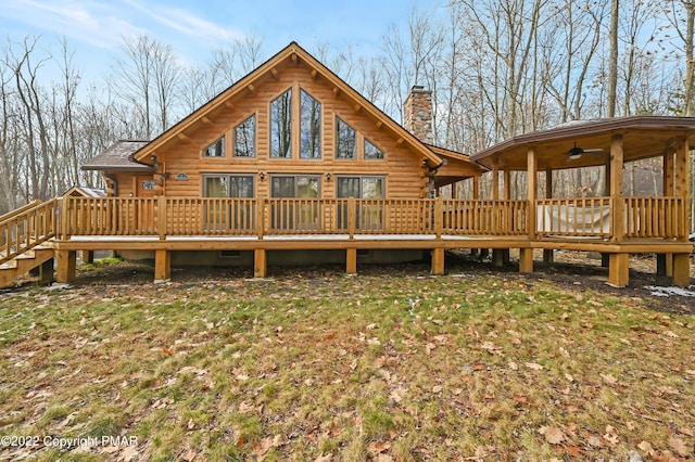 rear view of property featuring log exterior, a chimney, a wooden deck, and a lawn