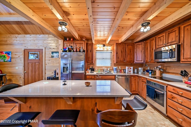 kitchen featuring stainless steel appliances, a breakfast bar, wood walls, a sink, and brown cabinetry