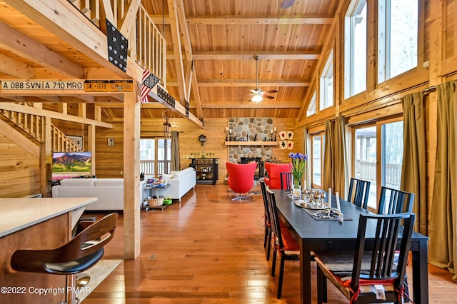 dining space with wood walls, a fireplace, wood ceiling, a wealth of natural light, and beam ceiling