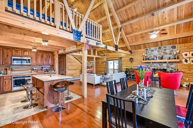 dining space with beam ceiling, a fireplace, light wood-style floors, wooden walls, and wooden ceiling