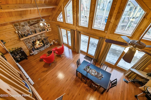 living area with beam ceiling, a fireplace, a ceiling fan, wood walls, and wooden ceiling