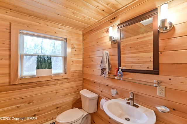 bathroom with wood walls, wooden ceiling, a sink, and toilet