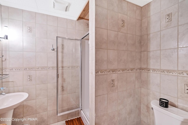 bathroom featuring a stall shower, a sink, tile walls, and toilet