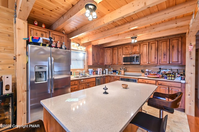 kitchen featuring brown cabinetry, appliances with stainless steel finishes, a center island, a sink, and beam ceiling