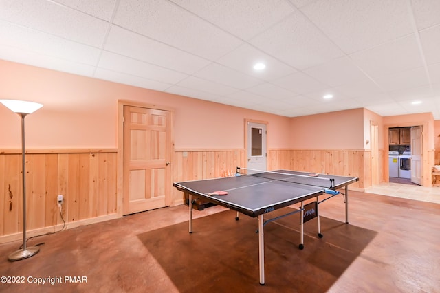 game room featuring wooden walls, a paneled ceiling, wainscoting, and finished concrete flooring