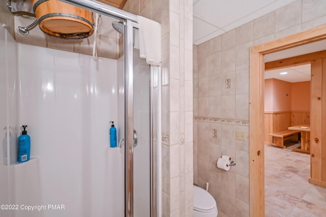 full bath featuring toilet, a stall shower, and tile walls