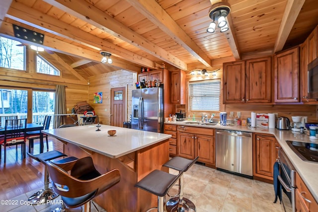 kitchen featuring wooden walls, appliances with stainless steel finishes, brown cabinetry, and light countertops