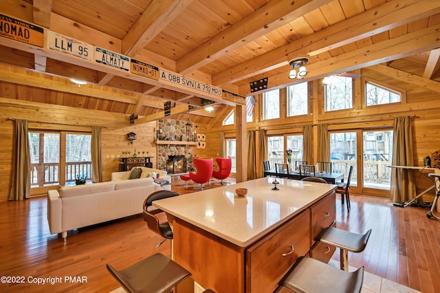 kitchen with lofted ceiling with beams, a stone fireplace, wooden ceiling, and wooden walls