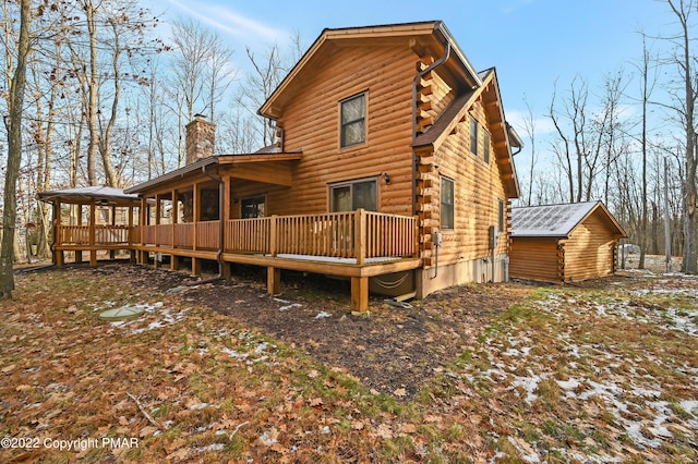 rear view of property featuring a deck, a chimney, an outdoor structure, and log exterior