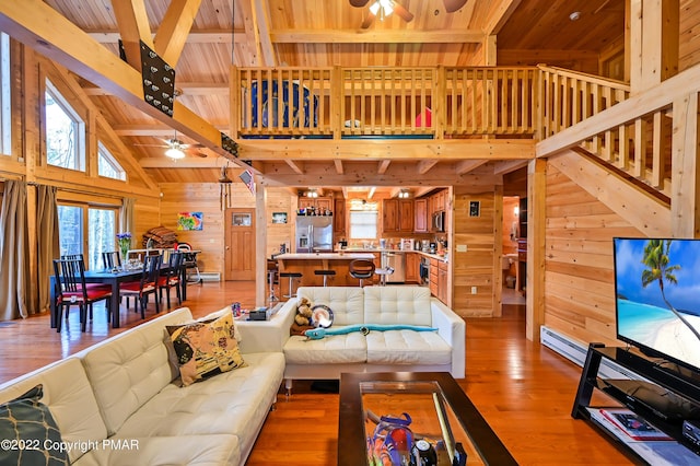 living area featuring ceiling fan, wood walls, wood ceiling, light wood-style floors, and beamed ceiling