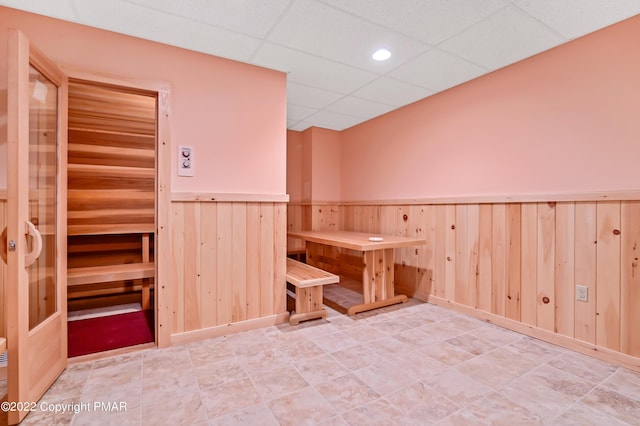 interior space with wood walls, a drop ceiling, and wainscoting