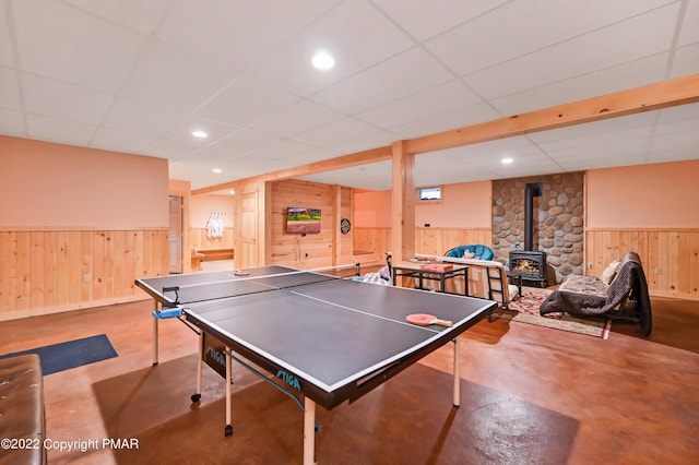 recreation room with a paneled ceiling, recessed lighting, concrete floors, wainscoting, and a wood stove