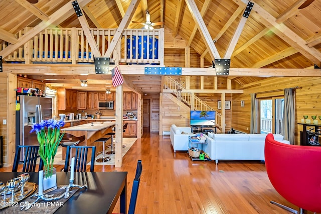 living room with light wood-style floors, ceiling fan, wooden walls, wooden ceiling, and beamed ceiling