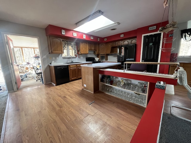 kitchen with a kitchen island, light countertops, light wood-style floors, black appliances, and a sink