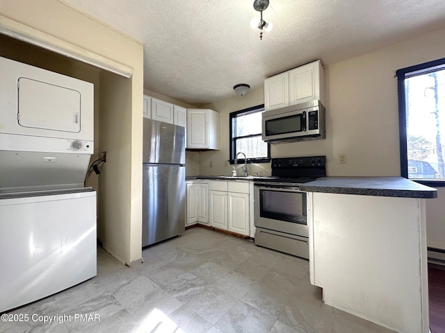 kitchen featuring a sink, stacked washer and dryer, appliances with stainless steel finishes, white cabinetry, and dark countertops