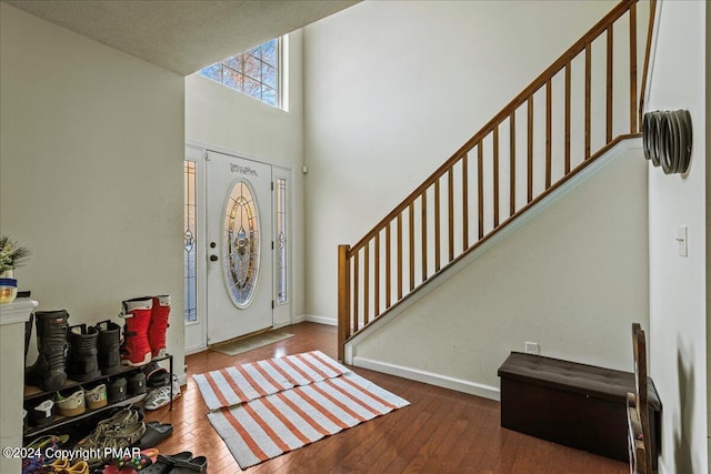 foyer entrance featuring wood-type flooring, a high ceiling, baseboards, and stairs