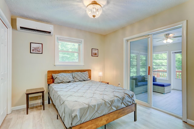 bedroom with a textured ceiling, wood finished floors, baseboards, access to exterior, and an AC wall unit