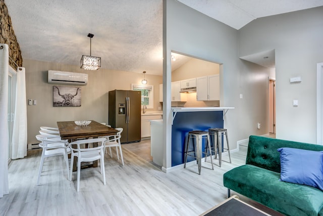 kitchen with stainless steel refrigerator with ice dispenser, lofted ceiling, an AC wall unit, under cabinet range hood, and a kitchen bar