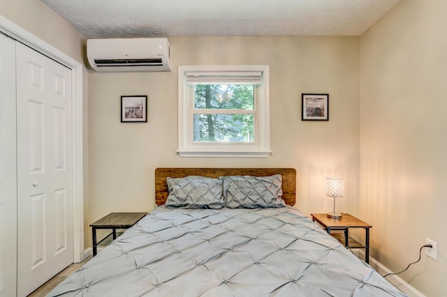 bedroom featuring a textured ceiling, a closet, a wall unit AC, and baseboards