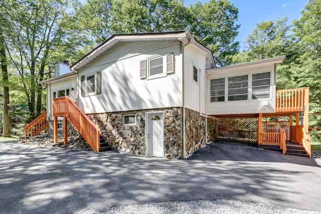 view of front of house featuring stone siding, stairway, aphalt driveway, and a sunroom