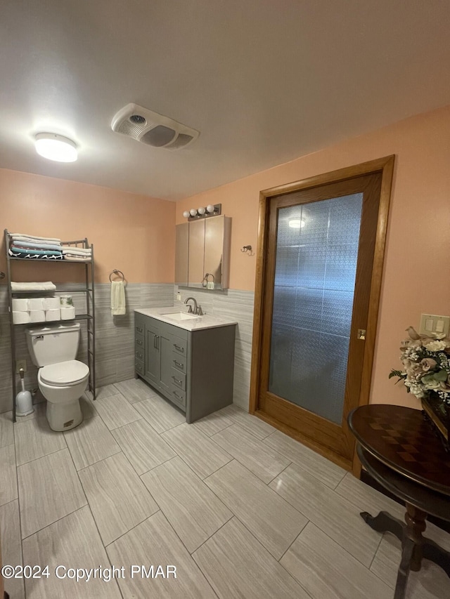 bathroom with vanity, a wainscoted wall, visible vents, tile walls, and toilet