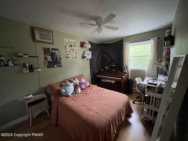 bedroom with a baseboard heating unit, wood finished floors, a wall mounted air conditioner, and ceiling fan