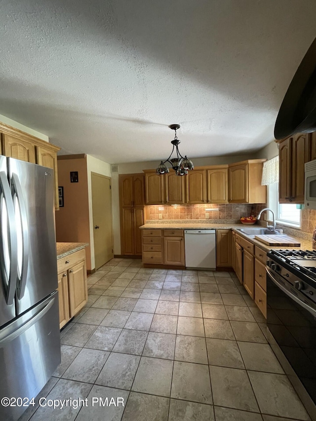 kitchen with a sink, light countertops, appliances with stainless steel finishes, pendant lighting, and tasteful backsplash