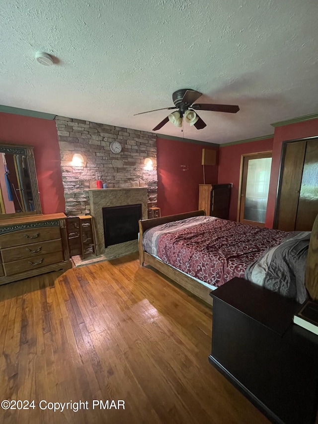 bedroom featuring ceiling fan, a textured ceiling, hardwood / wood-style floors, and a fireplace