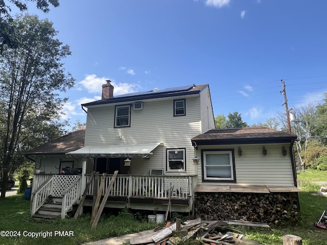 rear view of house featuring roof mounted solar panels, a deck, and a chimney