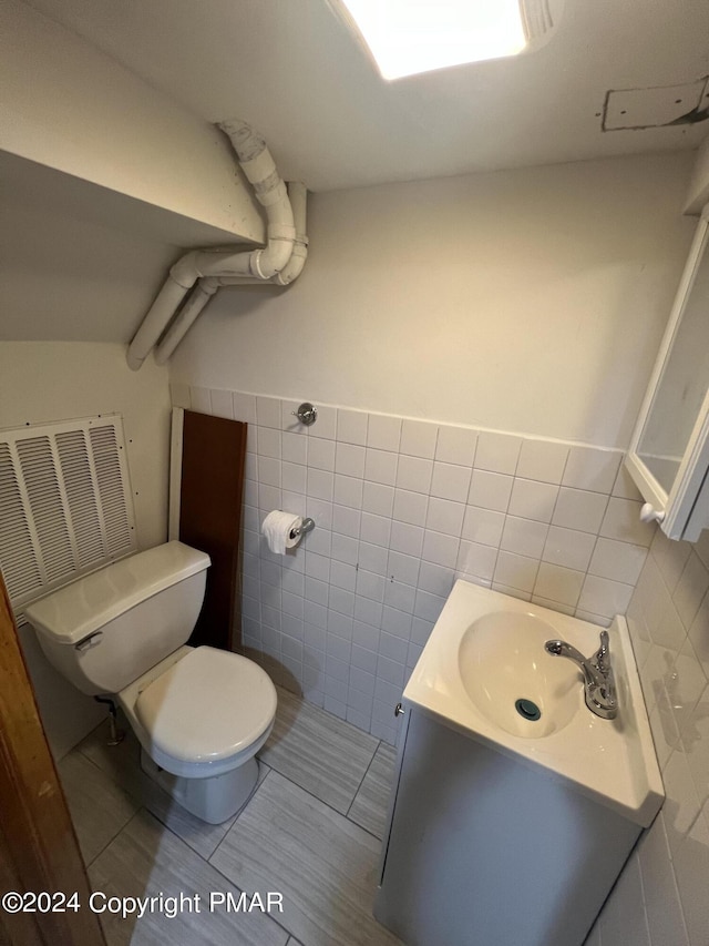 half bath with a wainscoted wall, toilet, tile walls, and vanity