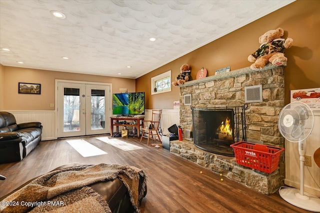 living area with a stone fireplace, wood finished floors, visible vents, french doors, and wainscoting