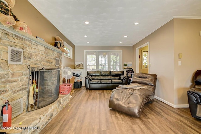 living area featuring ornamental molding, visible vents, a stone fireplace, and wood finished floors