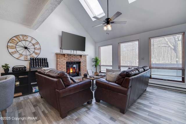 living room with a textured ceiling, high vaulted ceiling, light wood-style flooring, a fireplace, and a skylight