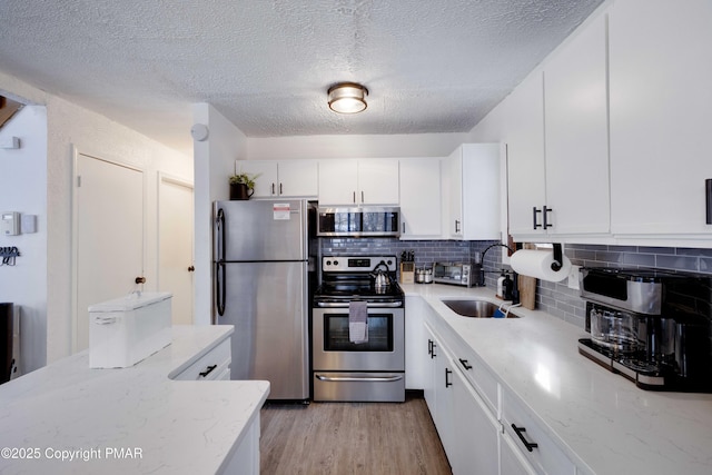 kitchen with light wood-style flooring, appliances with stainless steel finishes, a sink, white cabinetry, and backsplash