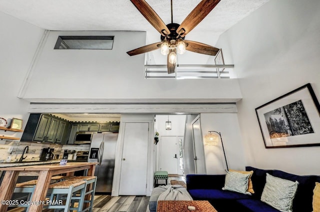 living room with a towering ceiling, ceiling fan, and light wood-type flooring