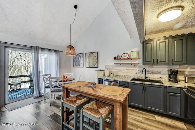 kitchen with pendant lighting, sink, vaulted ceiling, and light stone countertops