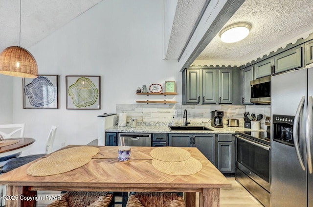 kitchen with appliances with stainless steel finishes, pendant lighting, sink, light stone countertops, and a textured ceiling