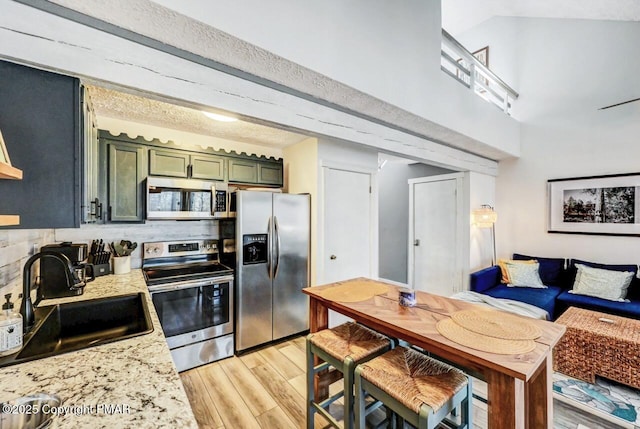 kitchen with sink, light hardwood / wood-style flooring, appliances with stainless steel finishes, light stone counters, and green cabinetry