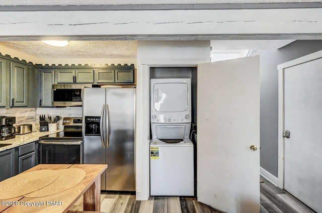 kitchen with stacked washer and dryer, wood-type flooring, appliances with stainless steel finishes, green cabinets, and light stone countertops