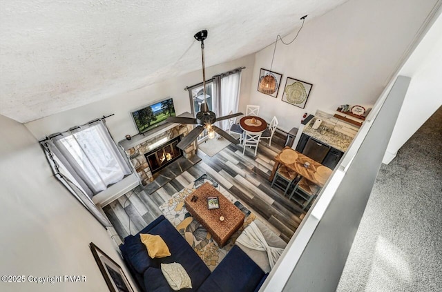 living room featuring lofted ceiling, a stone fireplace, a textured ceiling, and hardwood / wood-style flooring