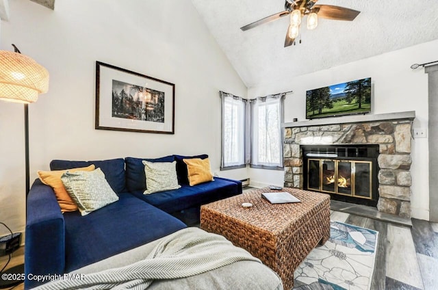 living room featuring lofted ceiling, ceiling fan, hardwood / wood-style floors, a textured ceiling, and a stone fireplace