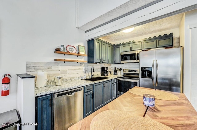 kitchen featuring sink, appliances with stainless steel finishes, light stone counters, green cabinetry, and decorative backsplash