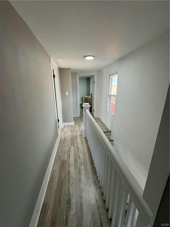 hall featuring an upstairs landing, baseboards, and light wood finished floors