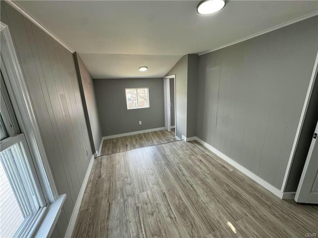 unfurnished bedroom featuring baseboards, wooden walls, crown molding, and wood finished floors