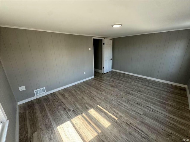 empty room featuring wood finished floors, ornamental molding, baseboards, and visible vents